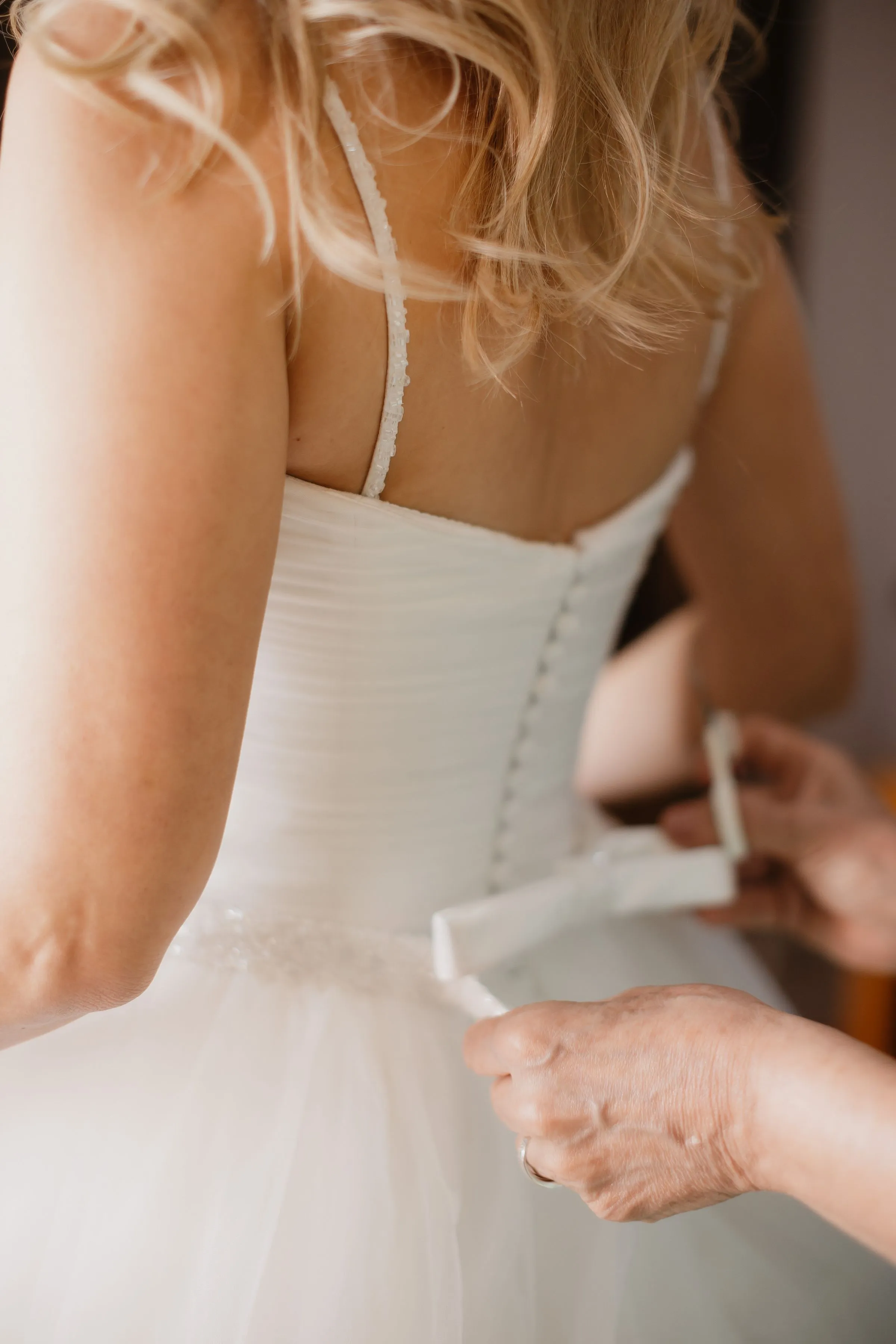 Hands fastening the buttons down the back of a wedding dress