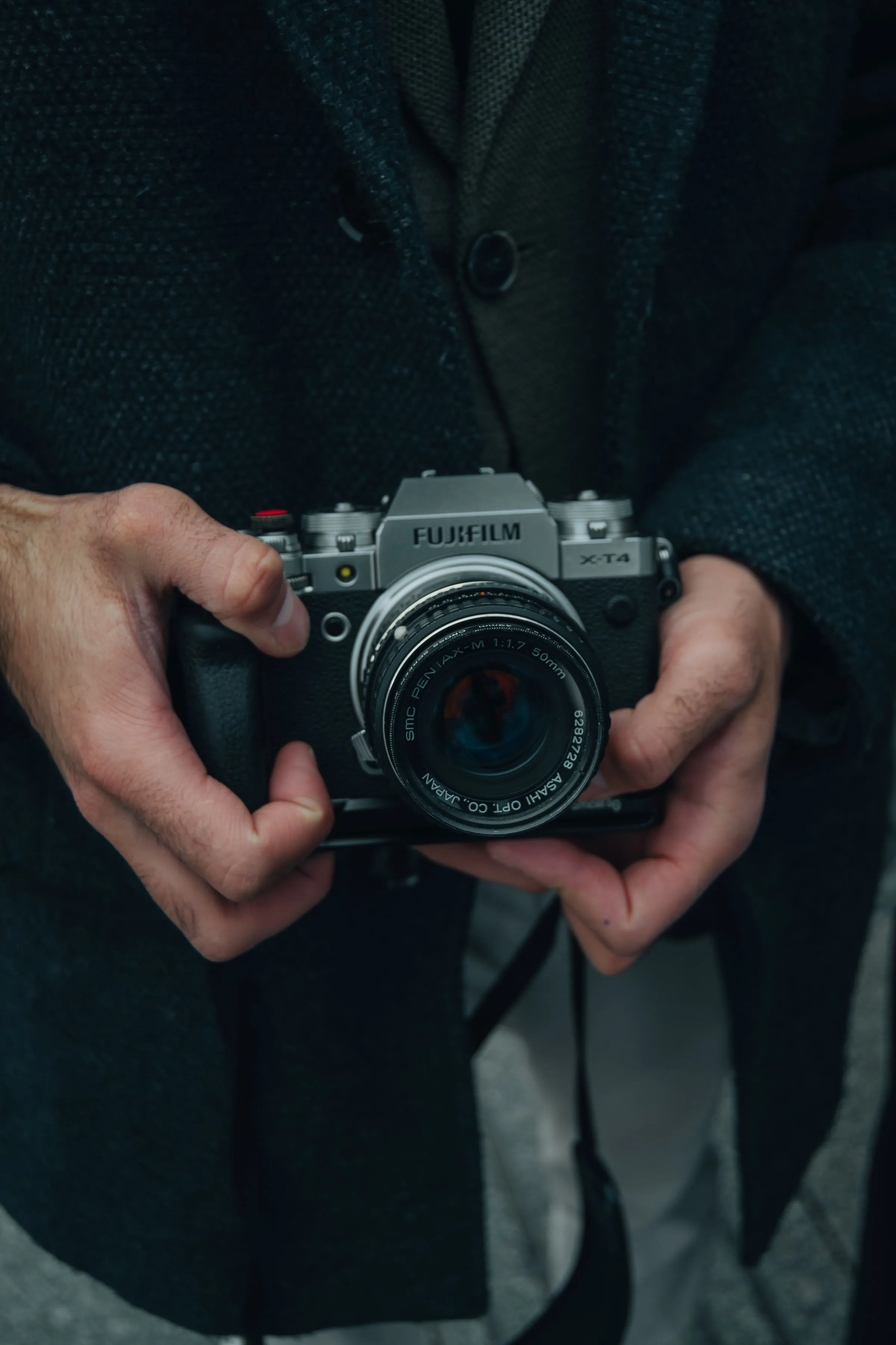 Hands holding a silver film-style camera against a dark coat