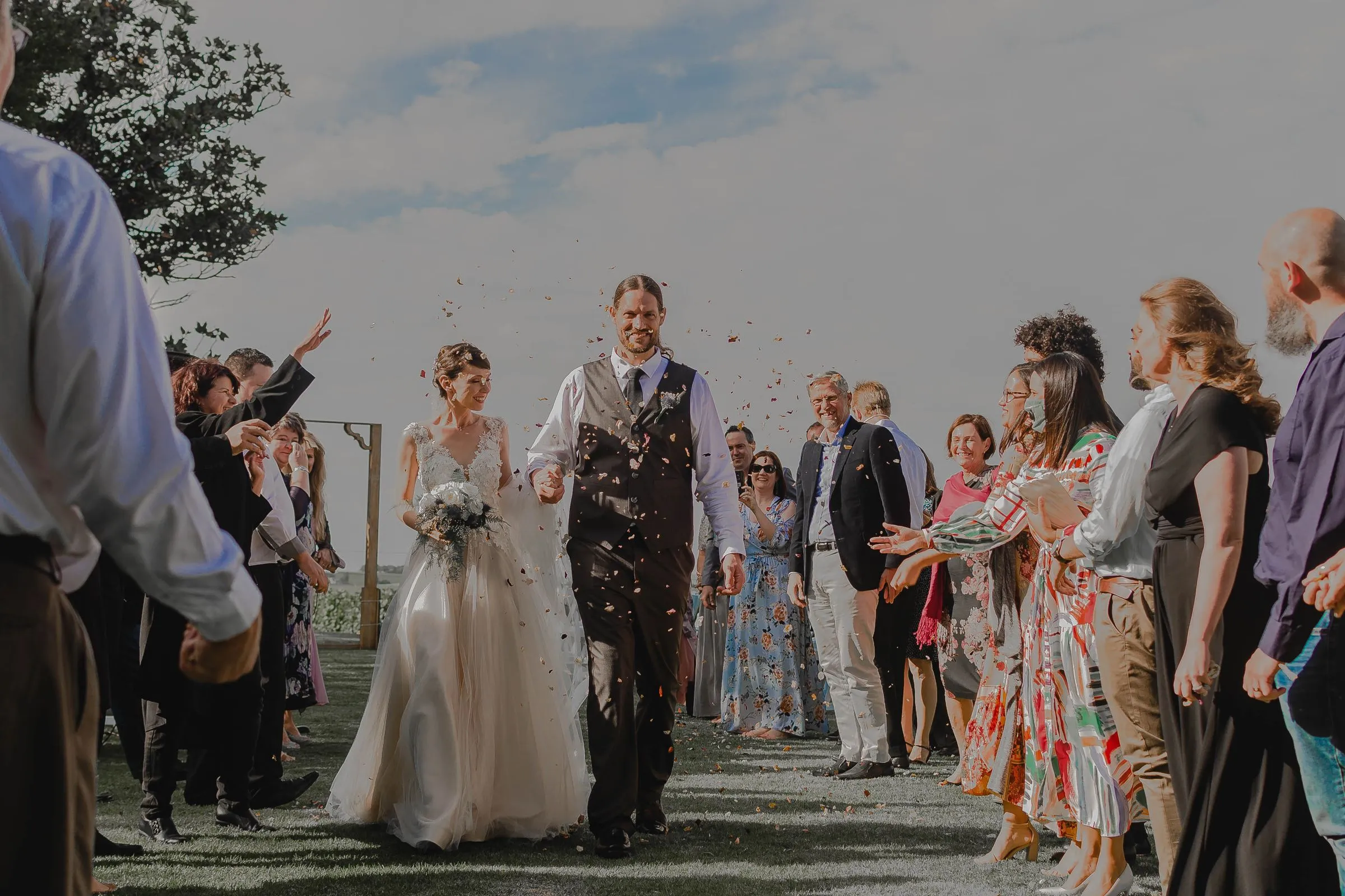 Guests throw confetti as the couple walk across a lawn