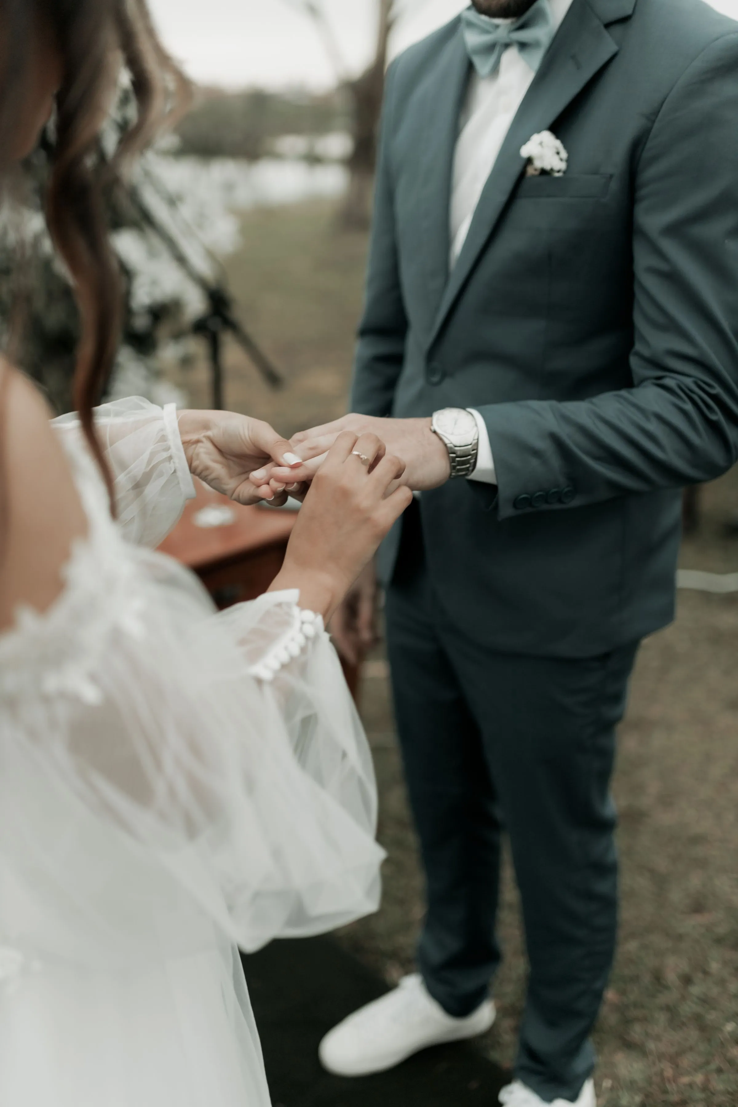 Close view of the groom sliding a ring onto the bride’s finger during an outdoor ceremony