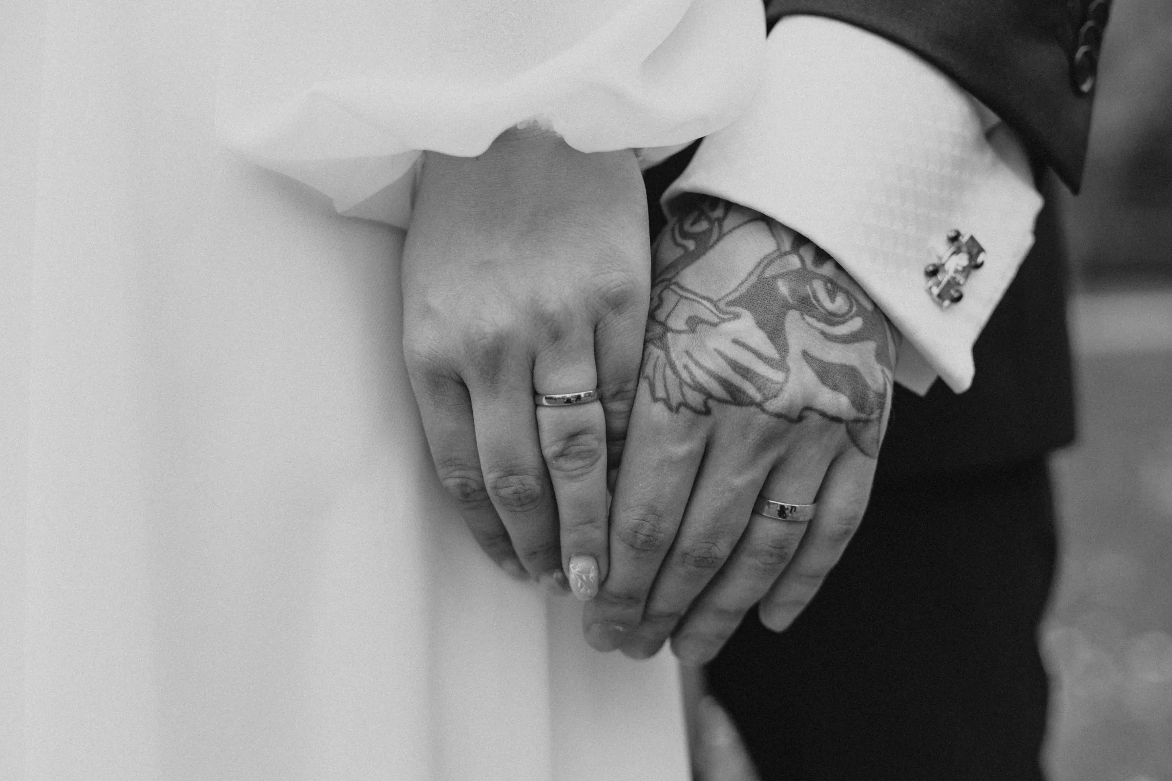Black and white close view of the couple’s hands with new rings, his arm tattooed